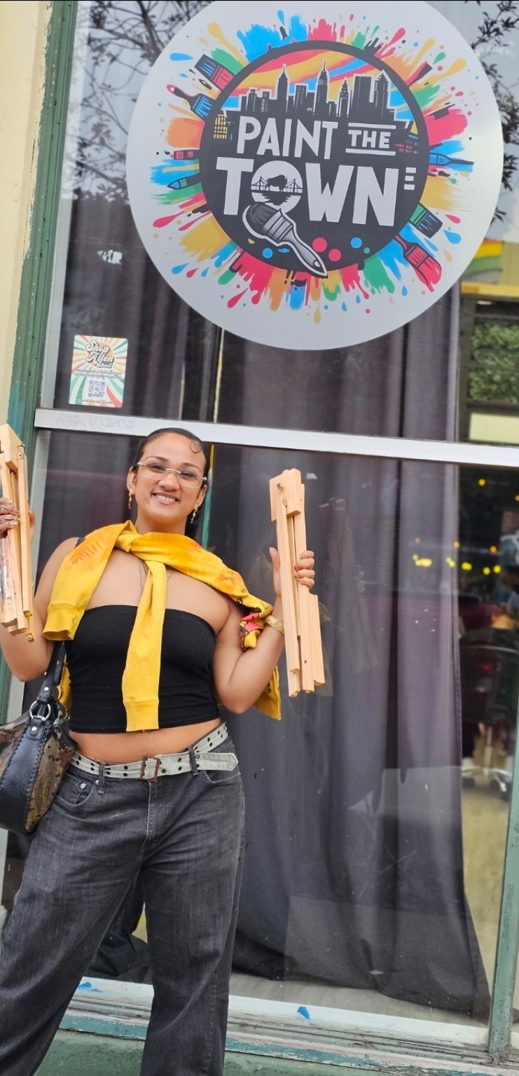 A community artist holding borrowed wooden easels outside Paint the Town